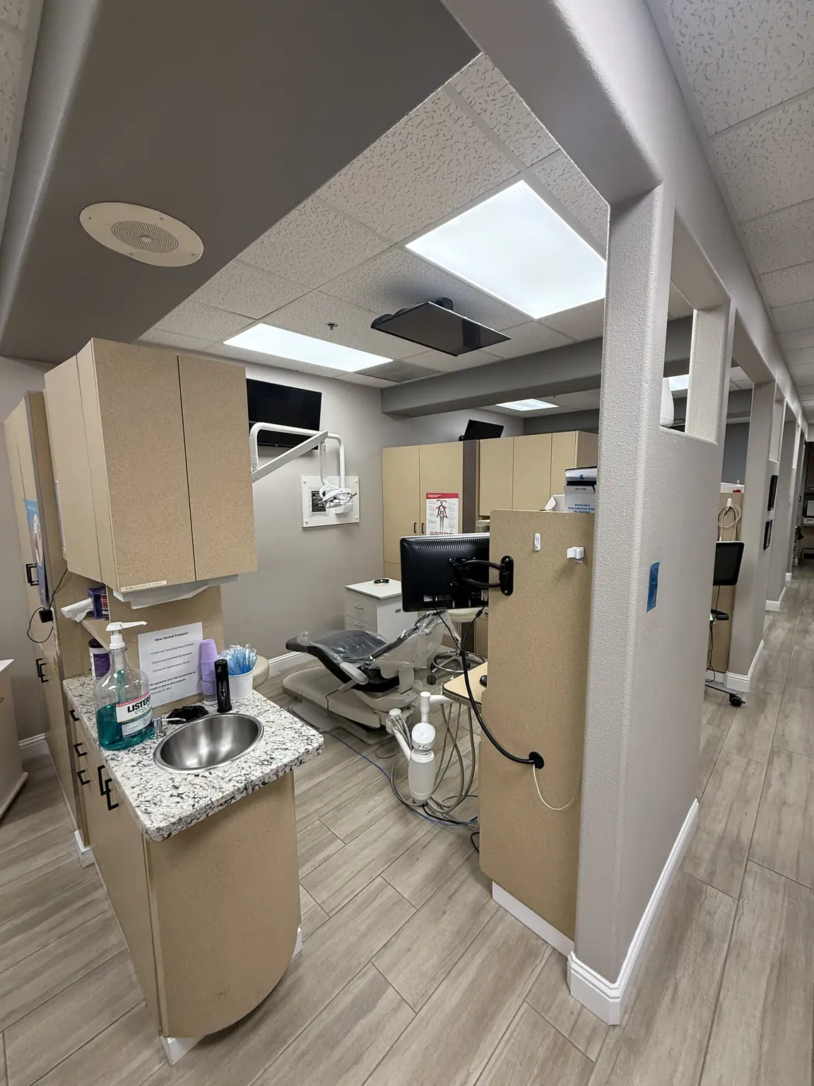 Treatment bay with a dental chair, sink station, and ceiling monitor